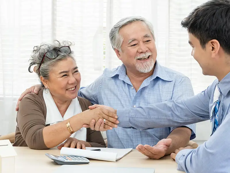 older man and woman smiling and shaking hands with business person