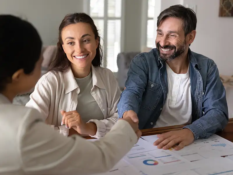 man and woman smiling and shaking hands with business person